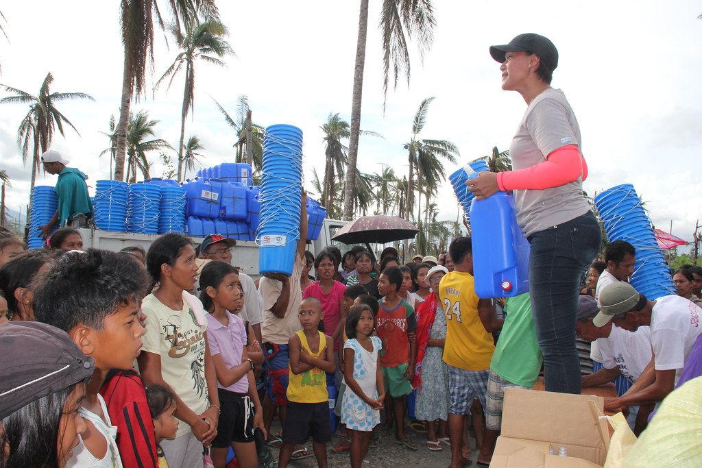 A volunteer handing out water containers to a crowd of children